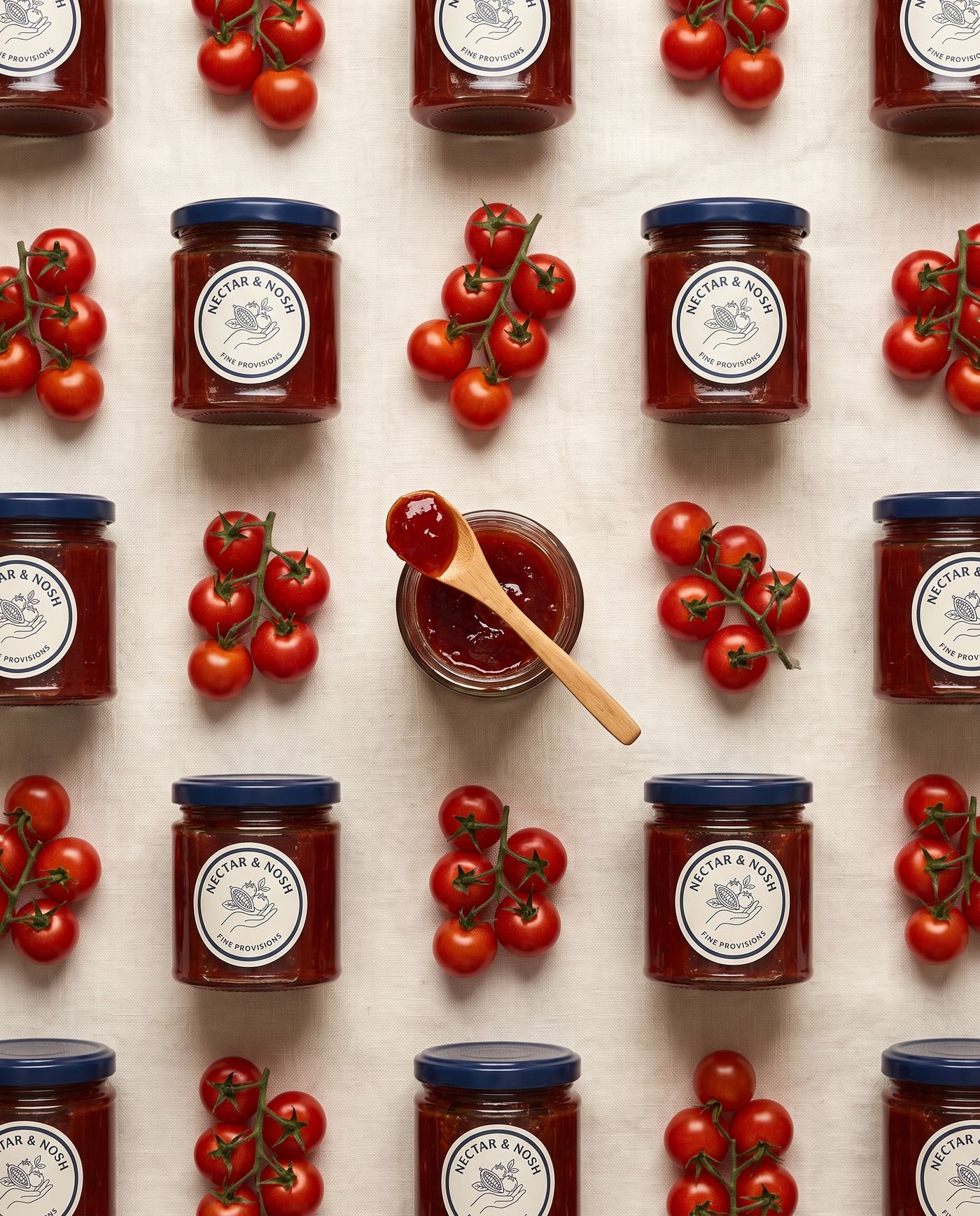 Top-down pattern of jam jars and vine tomatoes on cream linen